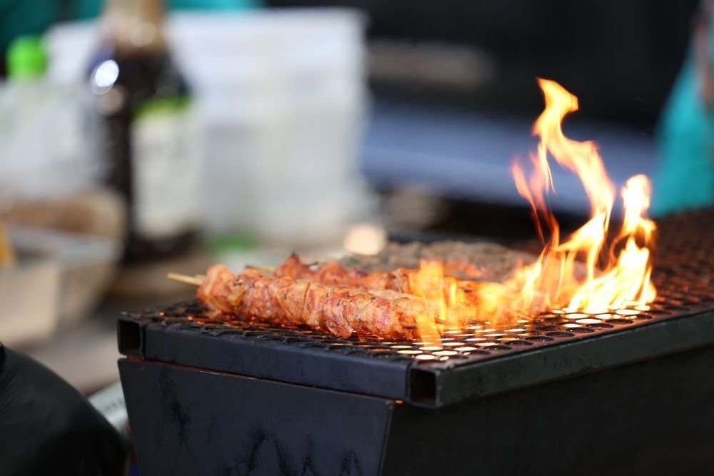 Row of meat skewers grilling over leaping flames on a small grill