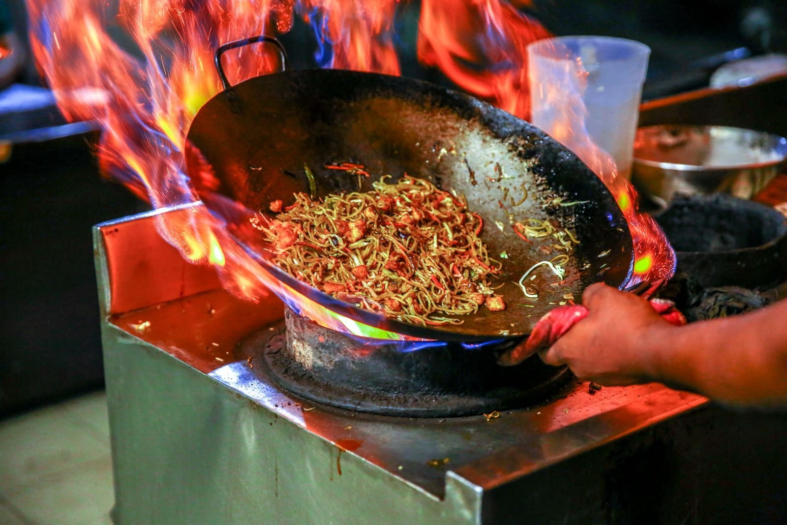 Wok of stir-fried noodles tossed over roaring burner flames