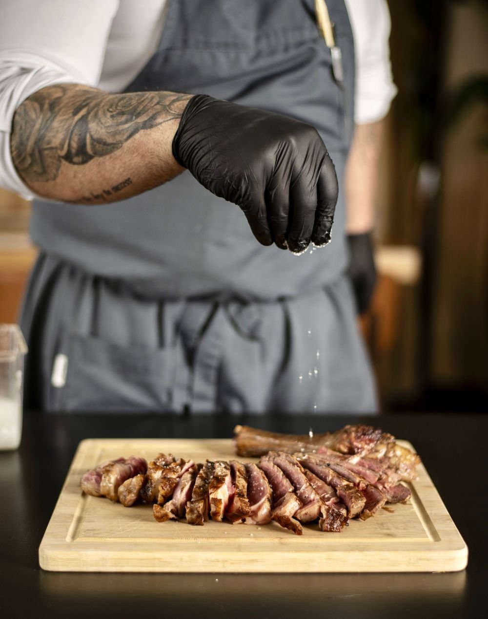 Cook in gloves seasoning sliced grilled steak on a cutting board