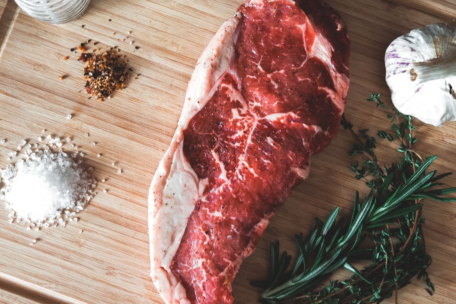 Raw strip steak on a wooden board with salt, garlic and rosemary