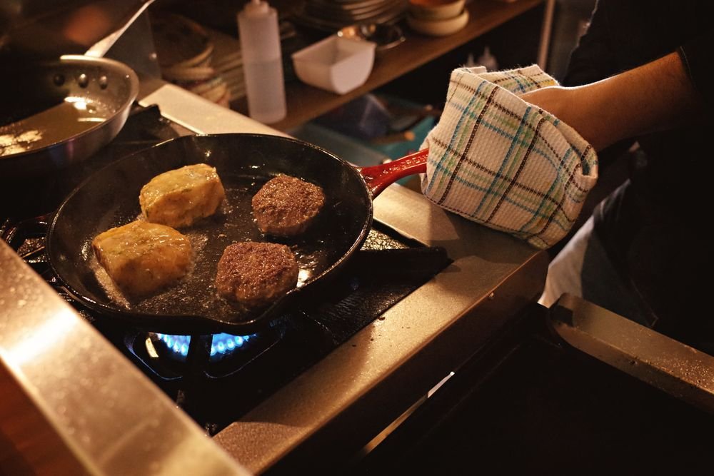 Breakfast patties and hash brown cakes frying in a cast iron pan