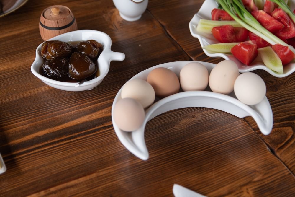 Brown eggs in a crescent dish beside tomatoes and scallions on wood