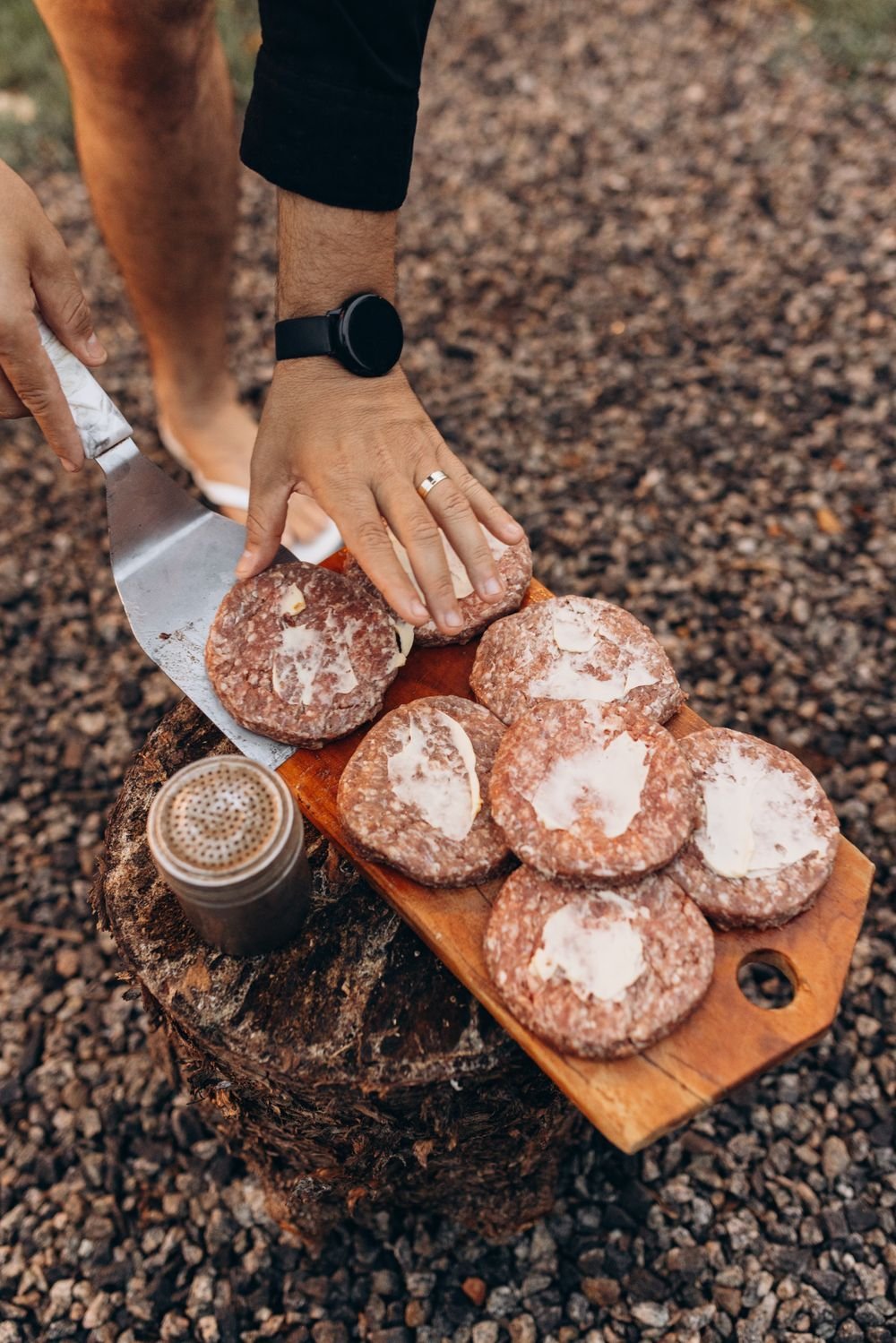 Hand pressing burger patties on a wooden board outdoors before grilling