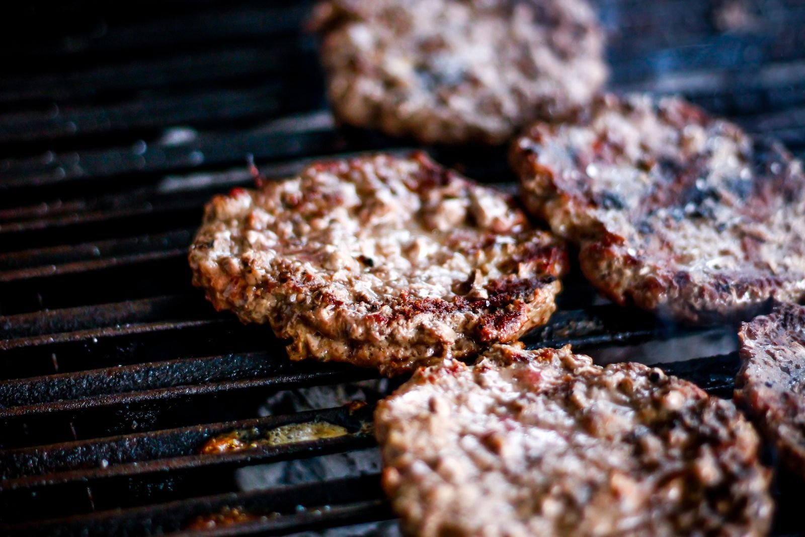 Charred beef burger patties sizzling on a hot grill grate