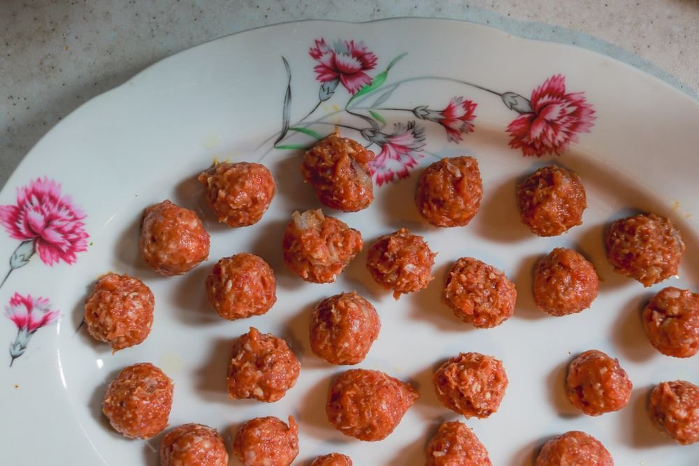 Rows of raw rolled meatballs on a floral china platter