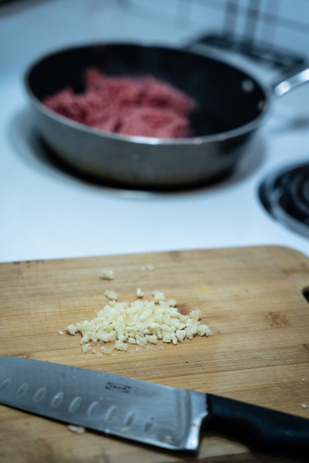 Ground beef in a skillet above minced garlic and a chef knife