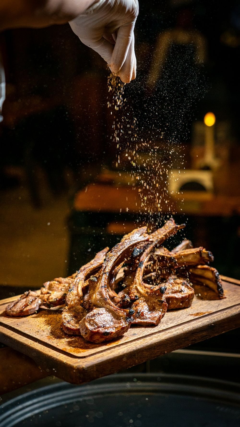 Seasoning sprinkled over seared frenched lamb chops on a wooden board