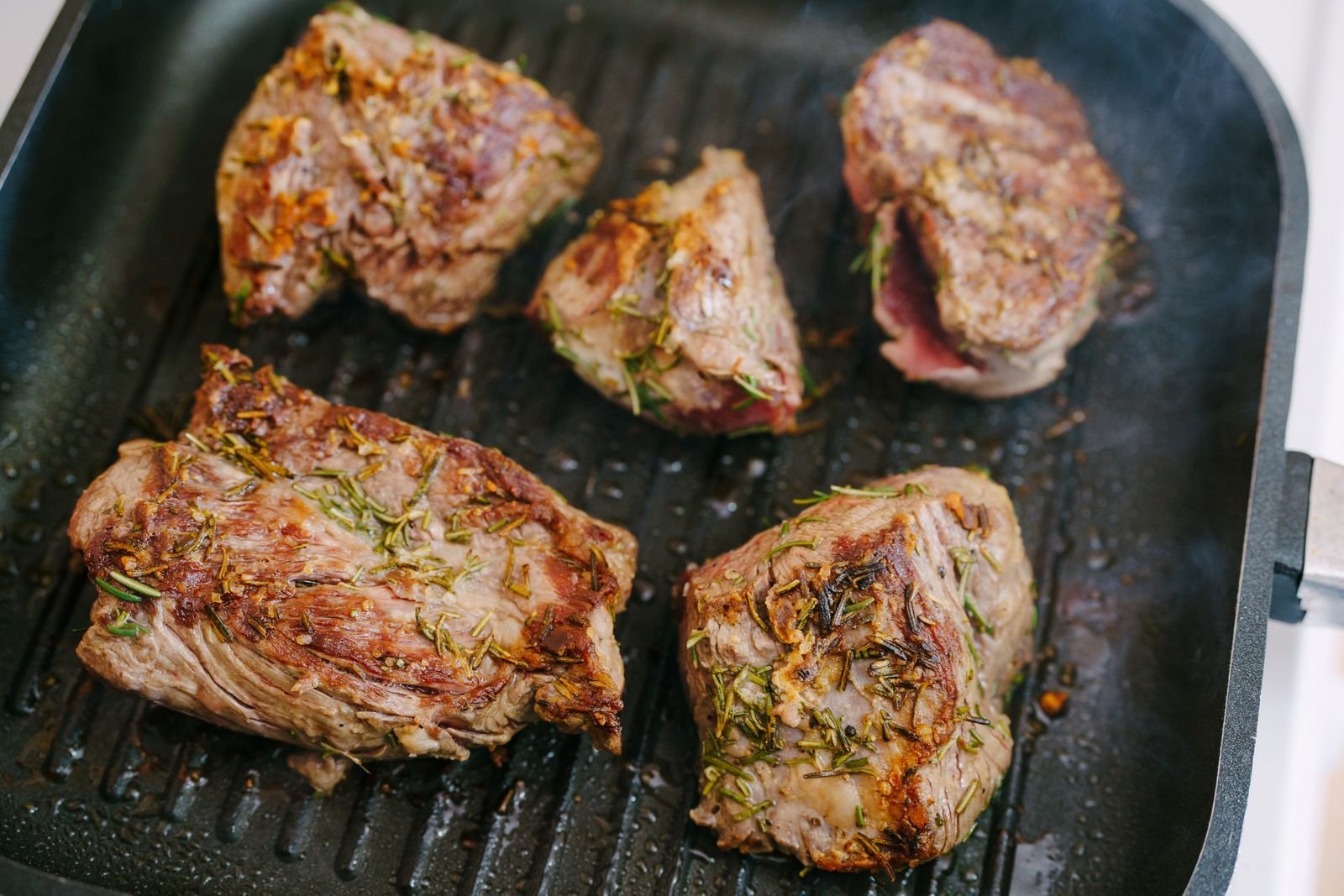 Rosemary-crusted lamb pieces searing in a black ridged grill pan