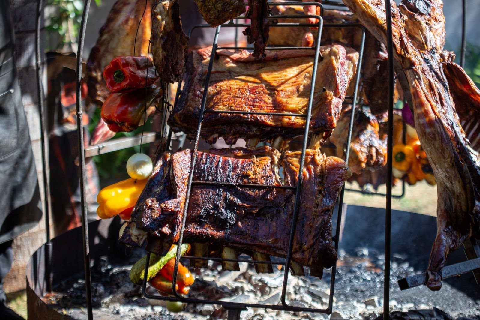 Asado ribs and whole cuts roasting in iron cages over glowing coals