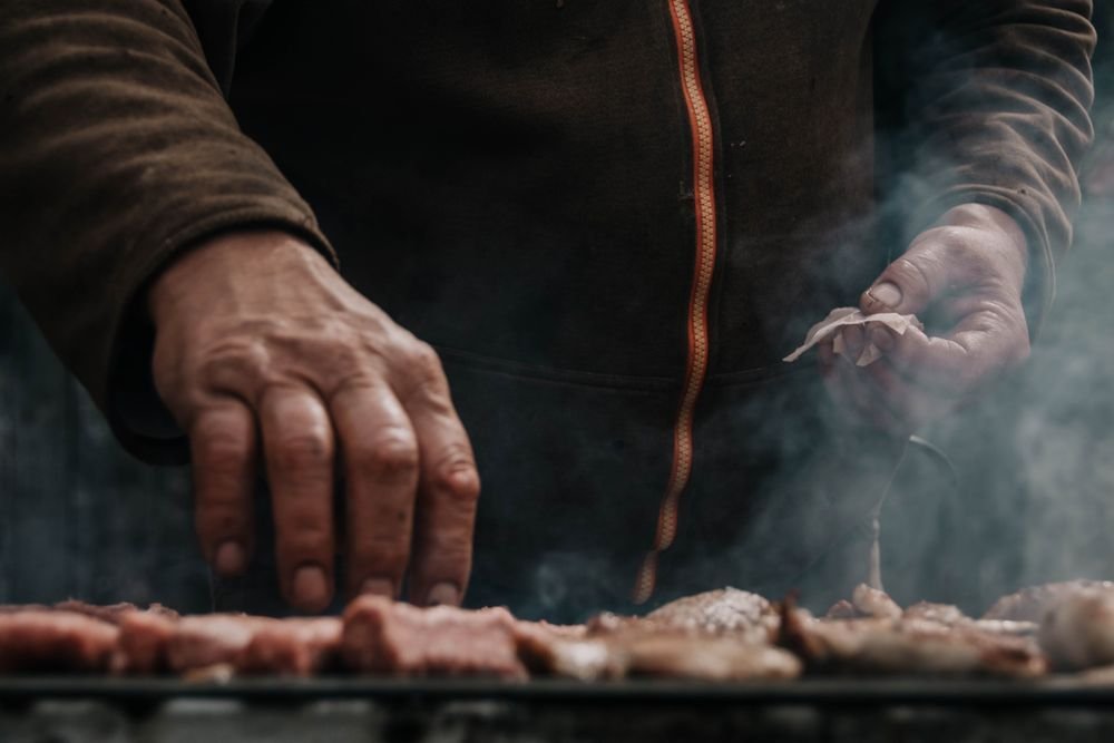 Hands turning pieces of meat on a grill through drifting smoke