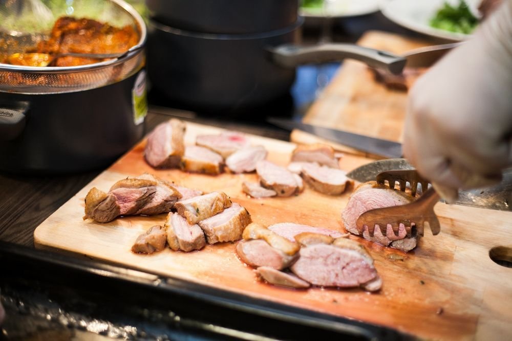 Hand slicing a rosy roasted pork tenderloin on a wooden board