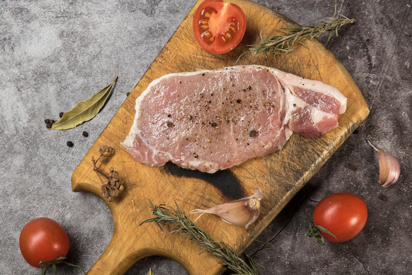 Seasoned raw pork chop on a cutting board with tomatoes and garlic
