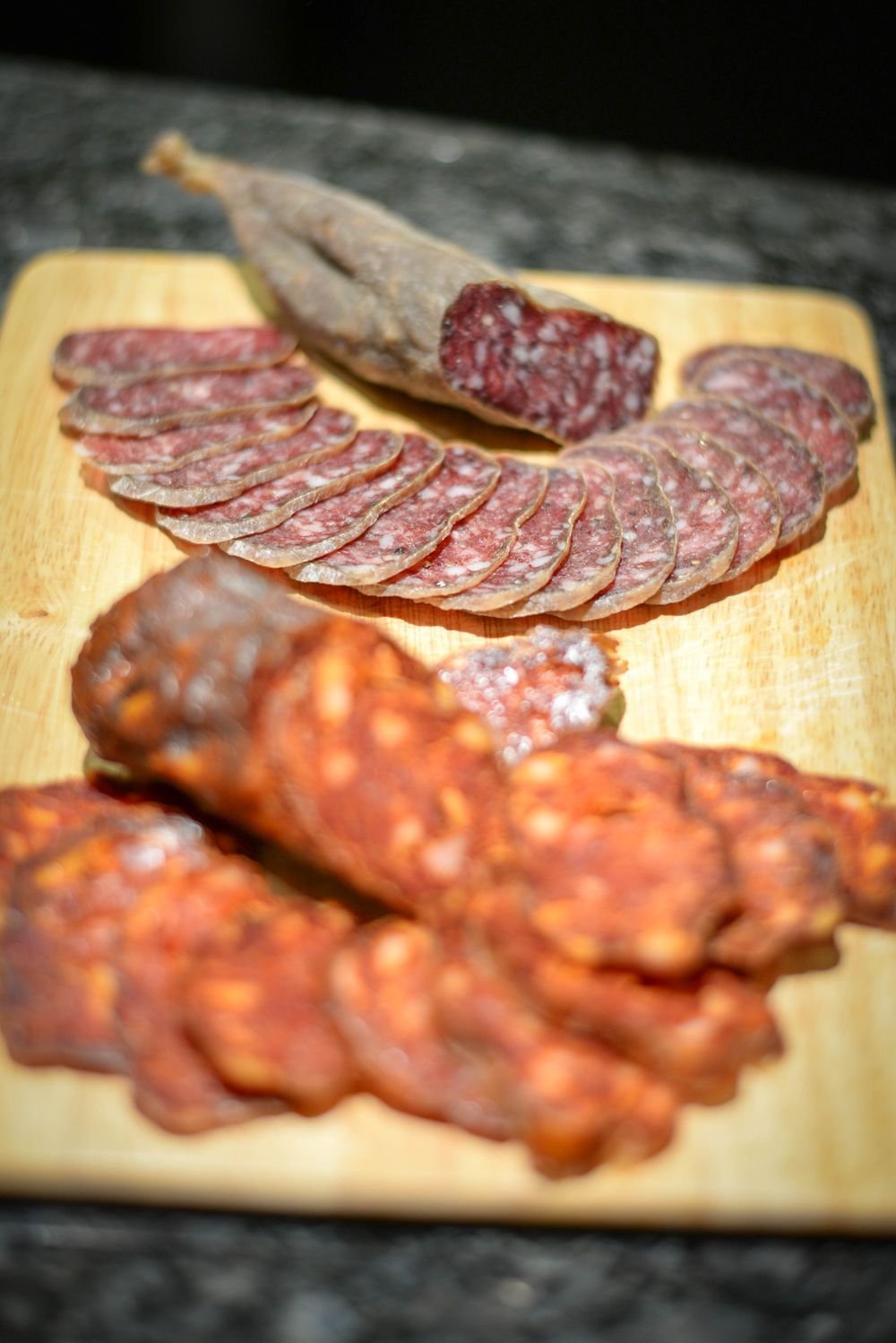 Sliced salami and chorizo fanned across a small wooden board