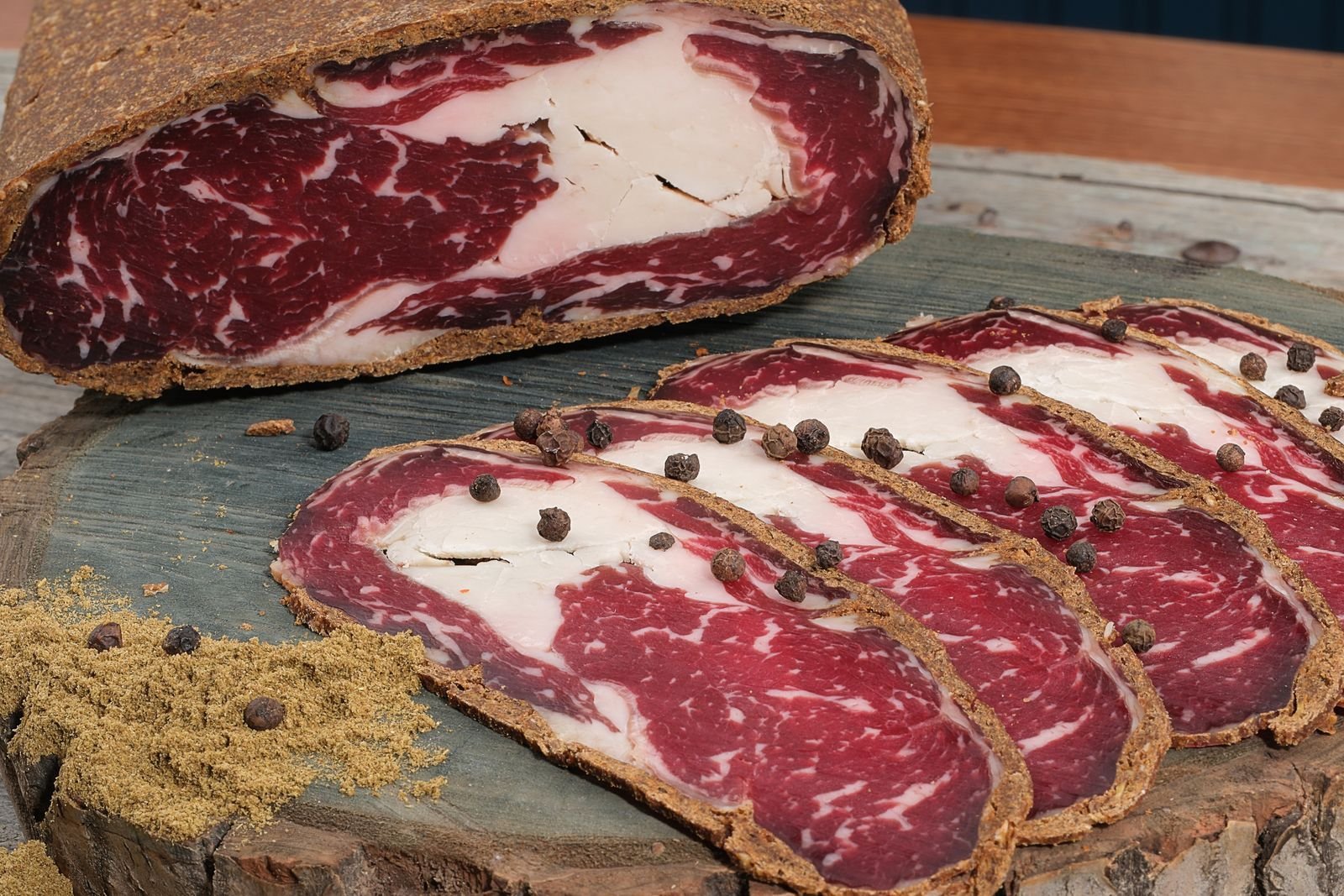 Thin slices of dry-cured beef with peppercorns on a wooden slab