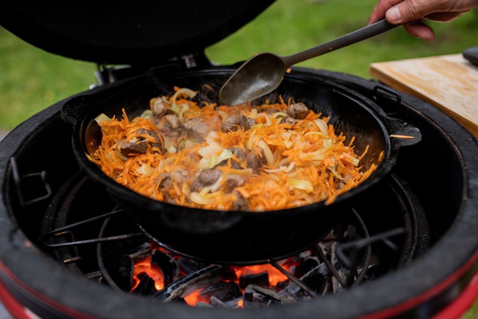 Cast iron pan of carrots, onions and mushrooms cooking over coals