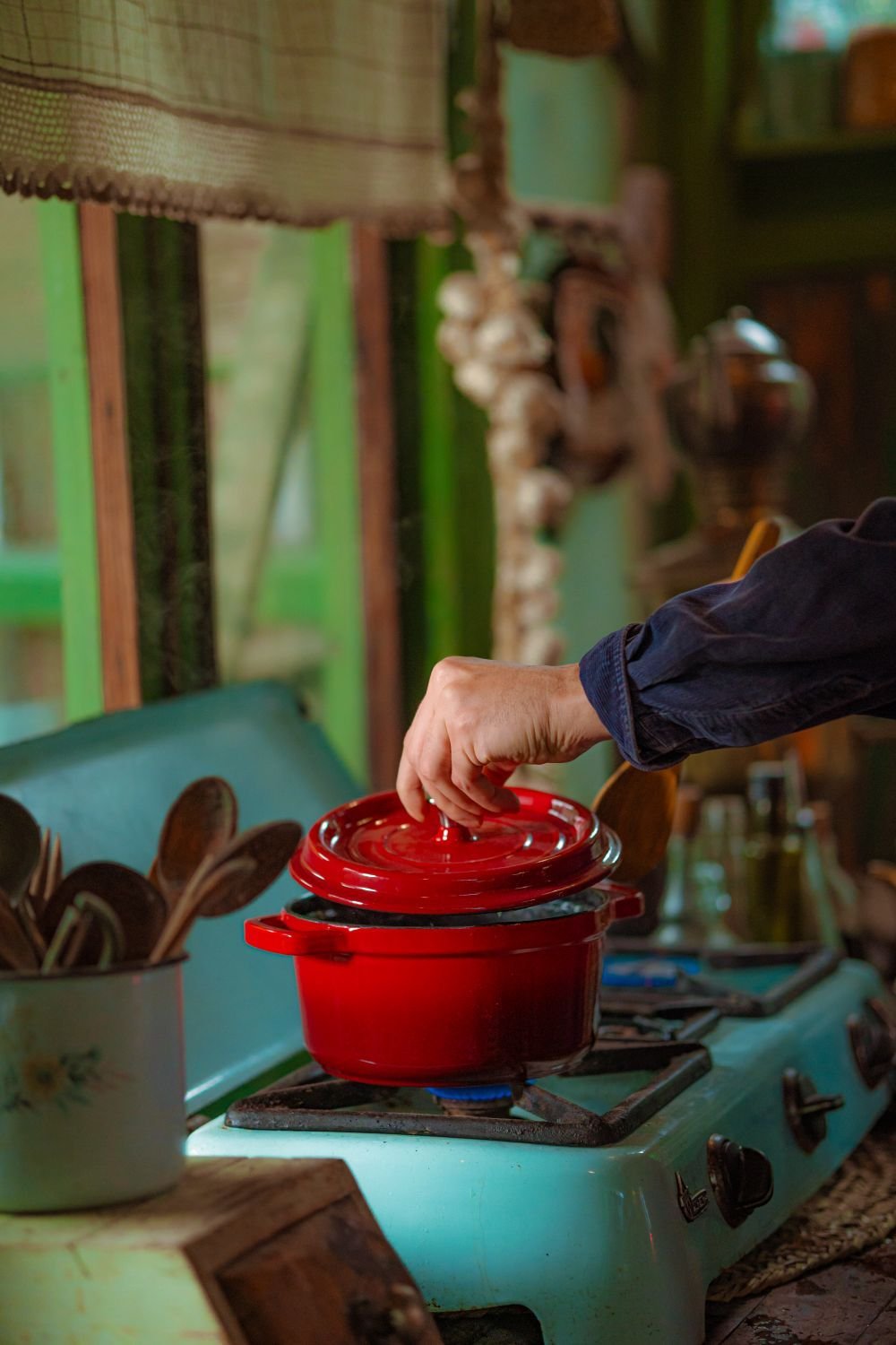 Hand lifting the lid of a red Dutch oven on a stove