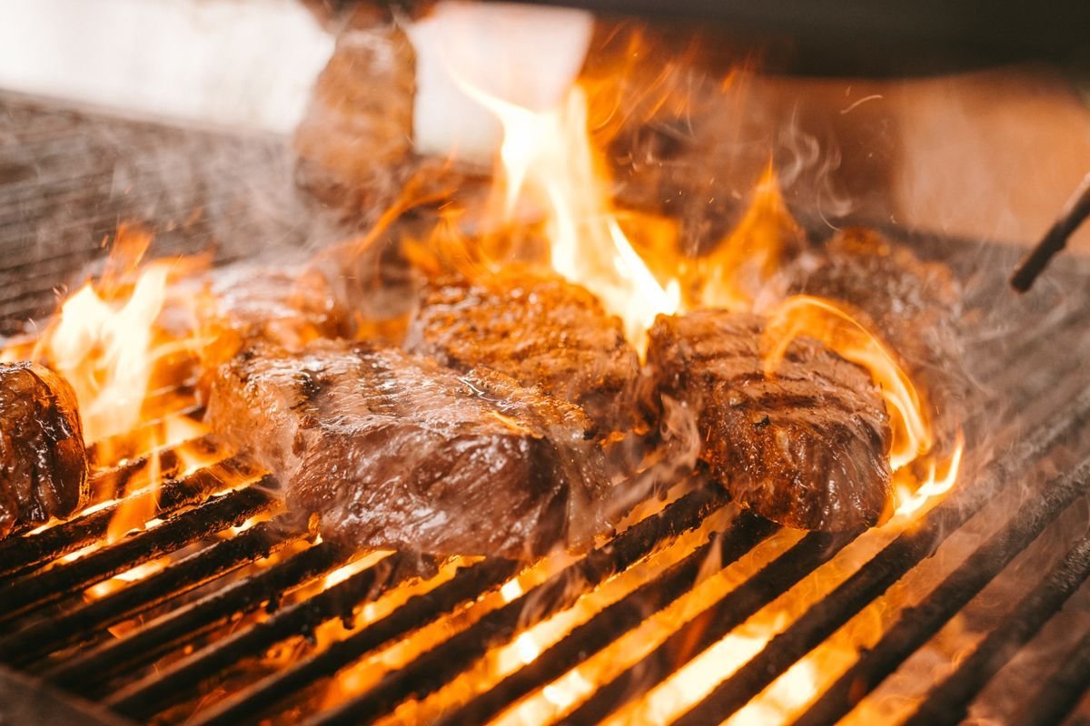 Thick steaks engulfed in orange flames on a heavy grill grate