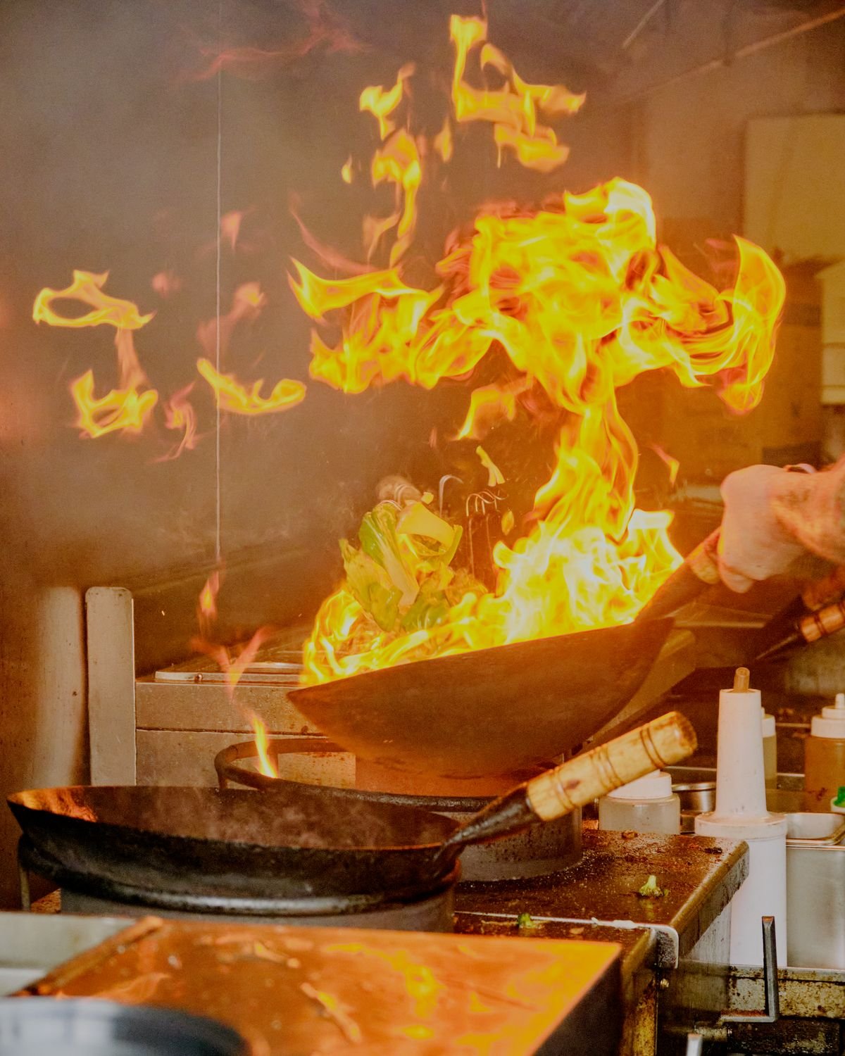 Tall burst of flame leaping from a wok in a busy kitchen