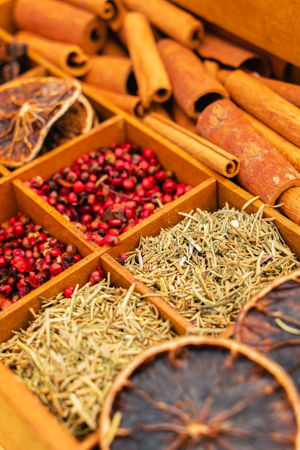 Wooden spice box with cinnamon sticks, pink peppercorns and dried rosemary