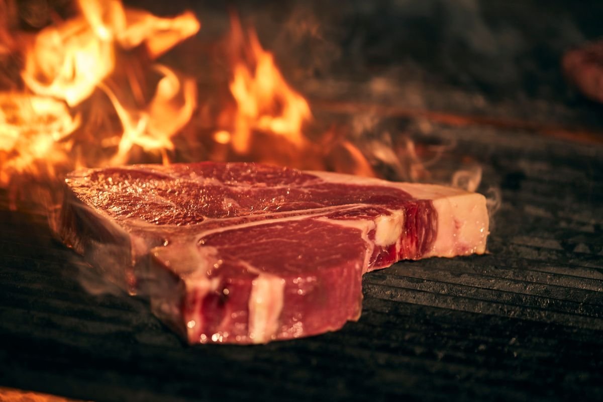 T-bone steak on a charred grate with flames rising behind